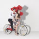 Models riding a bike and wearing gray suspenders holding heart balloons