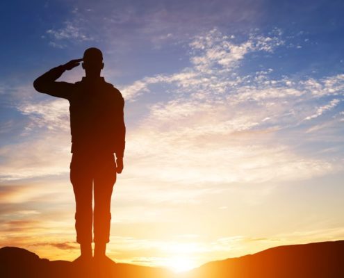 Rear view of soldier saluting at sunset